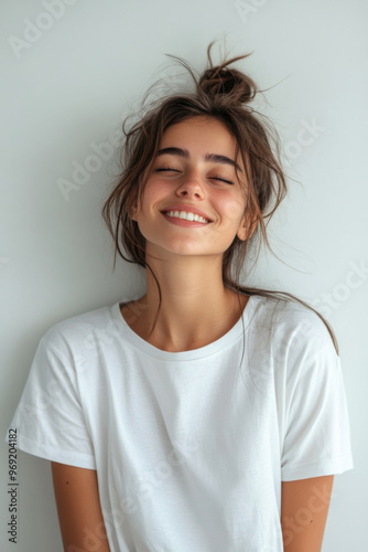 Happy Woman,  A cheerful woman wearing a loose white T-shirt poses against a plain white wall, expressing joy and positivity