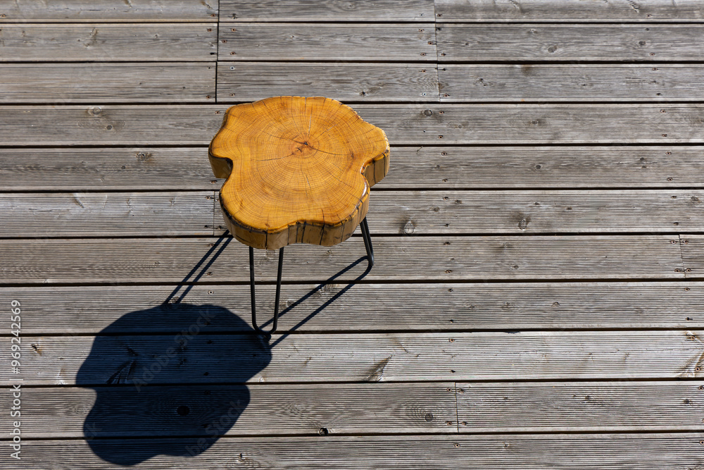 A coffe table made of a light wood trunk against the background of wooden terrace boards. The tree rings of the trunk are clearly visible. A shot of the table from above, taken on a sunny day.