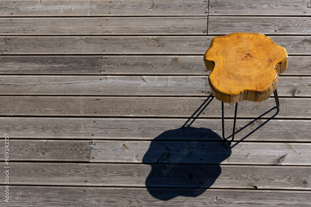 A coffe table made of a light wood trunk against the background of wooden terrace boards. The tree rings of the trunk are clearly visible. A shot of the table from above, taken on a sunny day.