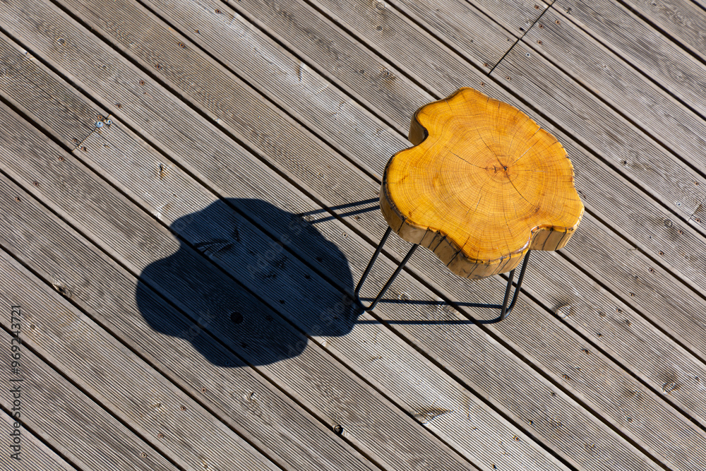 A coffe table made of a light wood trunk against the background of wooden terrace boards. The tree rings of the trunk are clearly visible. A shot of the table from above, taken on a sunny day.