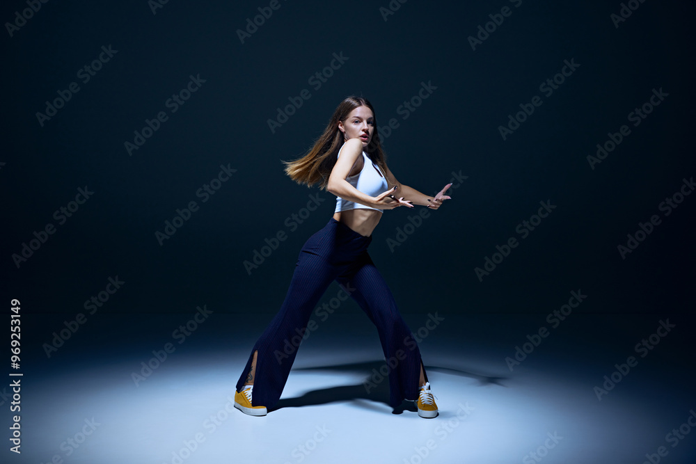 Obraz premium Youthful passion on display. Young energetic woman dancing hip hop with precision against navy blue studio background. Concept of freestyle dance, modernity, urban culture, youth