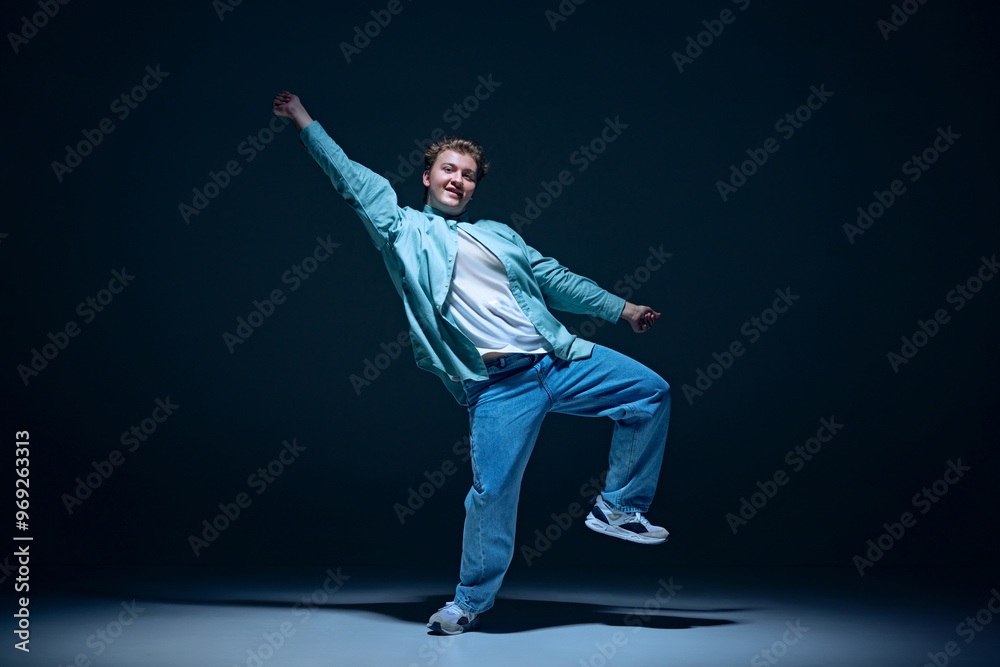 Artistic and joyful young man in casual clothes in motion on stage, performing hip hop against navy blue background. Concept of freestyle dance, modernity, urban culture, youth Artistic and joyful young man in casual clothes in motion on stage, performing hip hop against navy blue background. Concept of freestyle dance, modernity, urban culture, youth