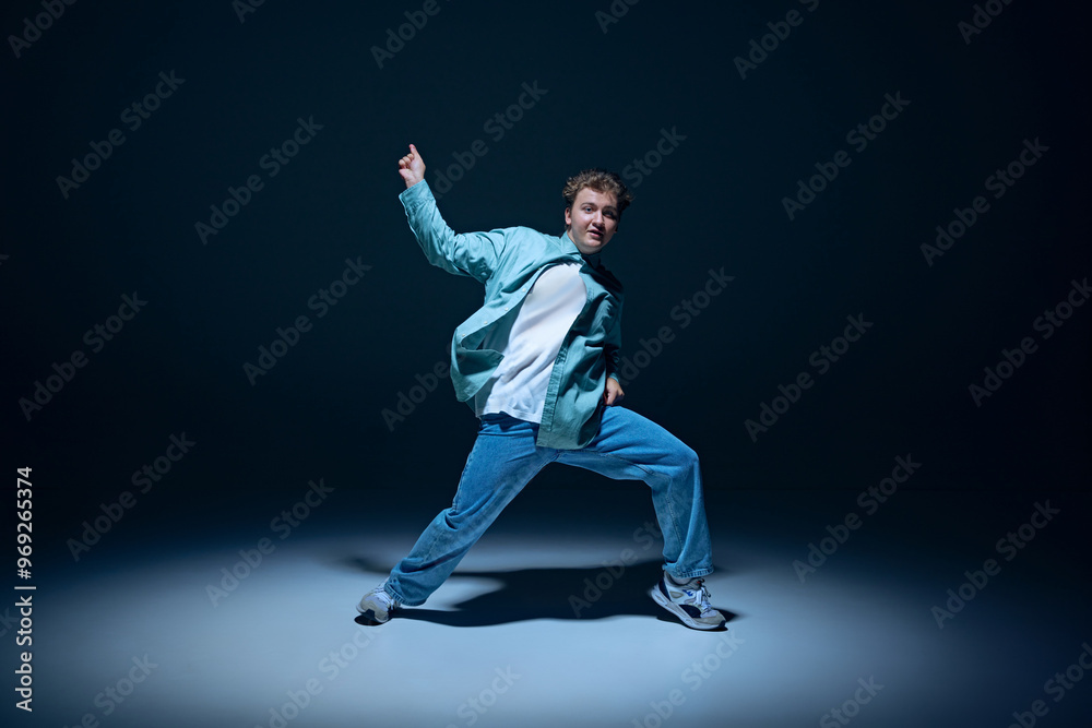 Stylish young guy, hip-hop dancer in motion on stage, training, performing with energy against navy blue background. Concept of freestyle dance, modernity, urban culture, youth Stylish young guy, hip-hop dancer in motion on stage, training, performing with energy against navy blue background. Concept of freestyle dance, modernity, urban culture, youth