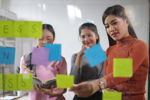 Startup business meeting, coworkers are discussing business project planning on transparent board and paper stickers in office. Group of women thinking to brainstorm and share ideas with colleagues.