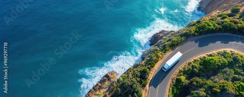 Aerial view of a white truck driving along a winding road by the ocean.