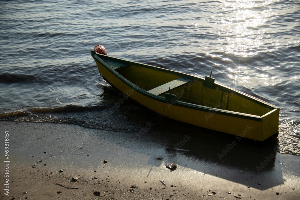 Yellow wooden boat on shore with sunlight reflecting on water Yellow wooden boat on shore with sunlight reflecting on water