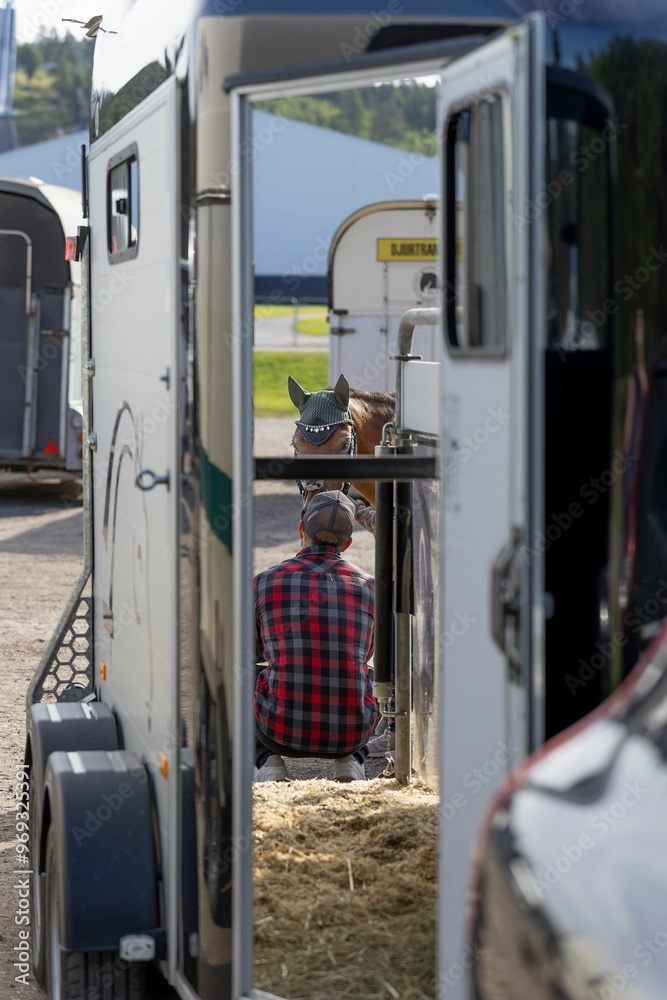 Man sitting beside a horse trailer with a horse in the background. Man sitting beside a horse trailer with a horse in the background.