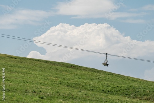 Ski lift over grassy hill with blue sky and clouds photo