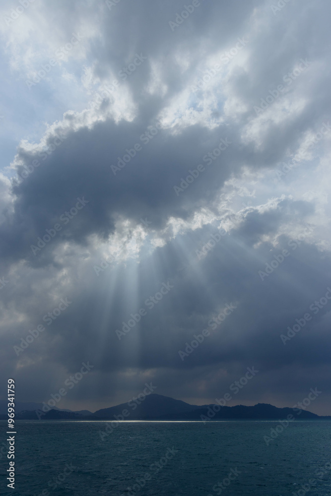 A serene moment unfolds as rays of sunlight break through dramatic clouds, illuminating the calm sea and distant mountains, creating a peaceful natural atmosphere A serene moment unfolds as rays of sunlight break through dramatic clouds, illuminating the calm sea and distant mountains, creating a peaceful natural atmosphere