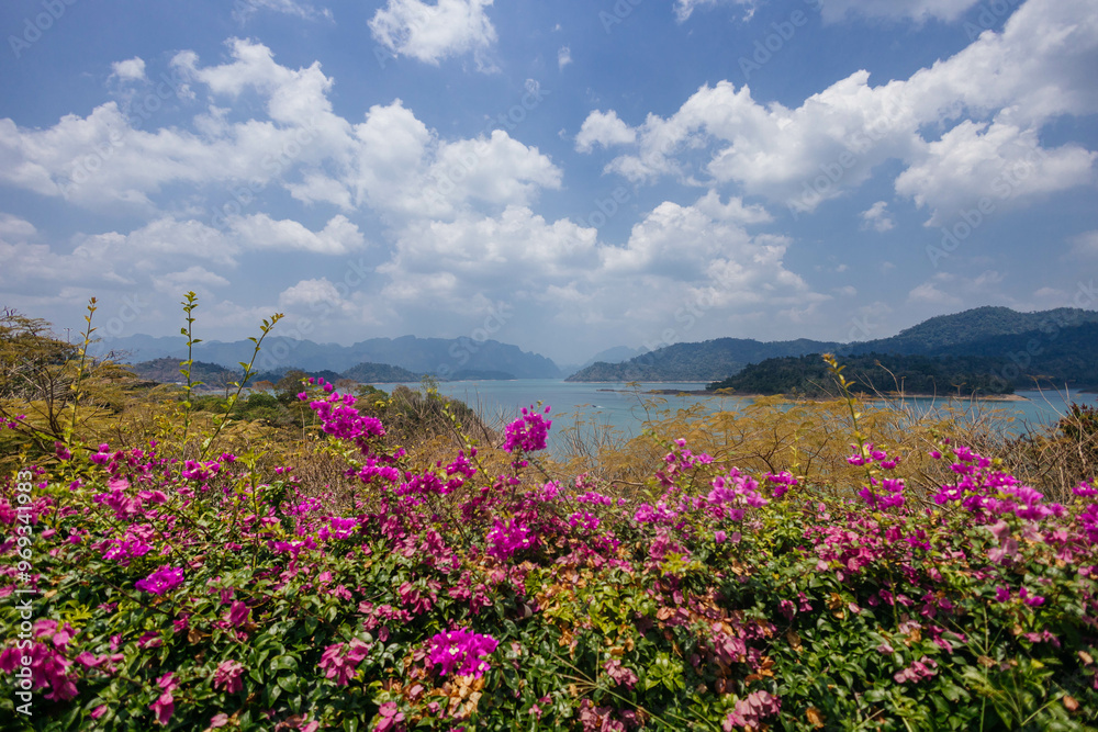 Obraz premium Colorful bougainvillea flowers thrive along the lake's edge, offering a beautiful contrast to the tranquil waters and distant mountains under a sunny sky