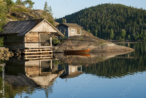 Obraz na plátně Scenic view of wooden cabins and a boat reflected in calm water in High coast Ar