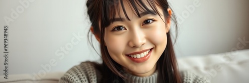 smiling asian woman with long hair and bangs sitting on a couch.