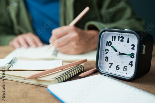 Valokuva A clock on the table with a man is writing on the notebook, writing and time con
