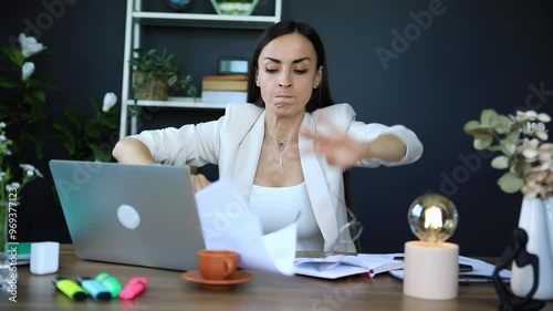Stressed young businesswoman with a headache holds her head in frustration while working at her laptop in a modern office. The scene of hard work, work-related stress, and concentration.