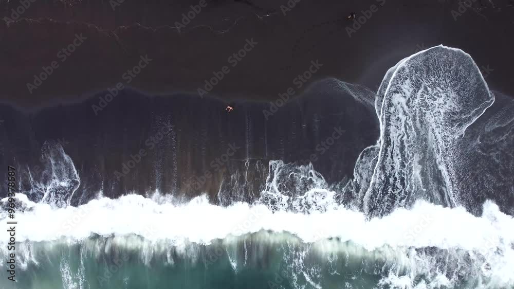 Aerial drone shot of a woman walking through the black sand beach in Acores, Portugal.