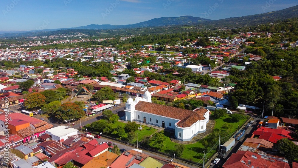 View of a colorful town with a prominent white church and surrounding green landscape View of a colorful town with a prominent white church and surrounding green landscape