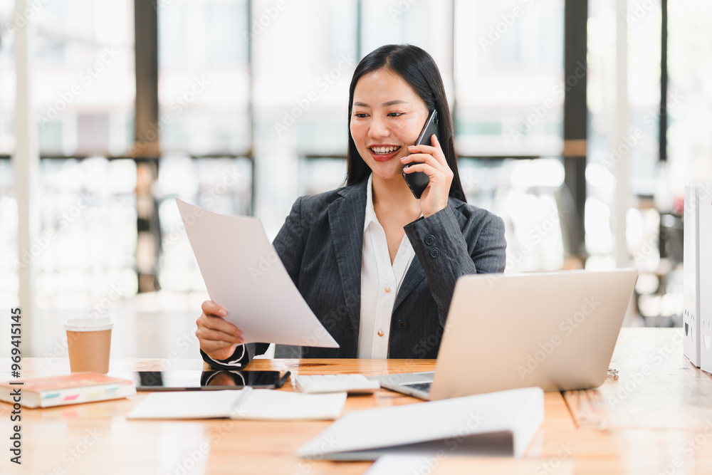 A professional woman smiles while talking on phone and reviewing documents A professional woman smiles while talking on phone and reviewing documents