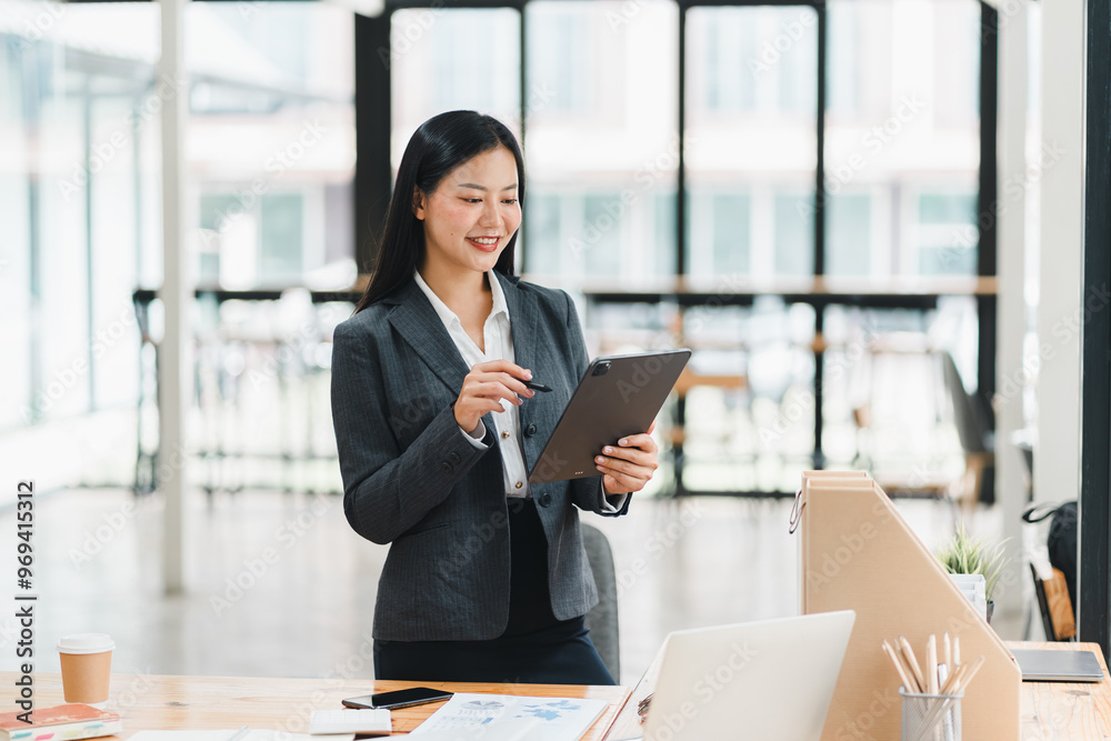 A professional woman in suit smiles while using tablet in modern office