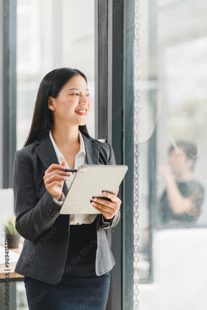 A confident businesswoman smiles while holding tablet in modern office A confident businesswoman smiles while holding tablet in modern office