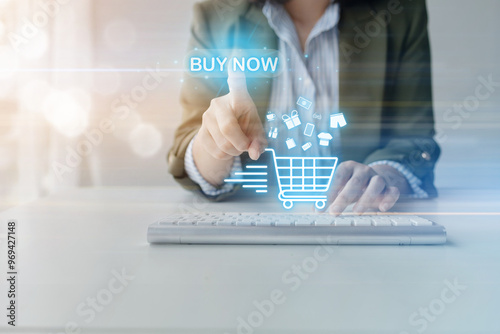 A woman is pointing at a shopping cart on a computer screen. The shopping cart is filled with various items, including clothes and a cell phone.