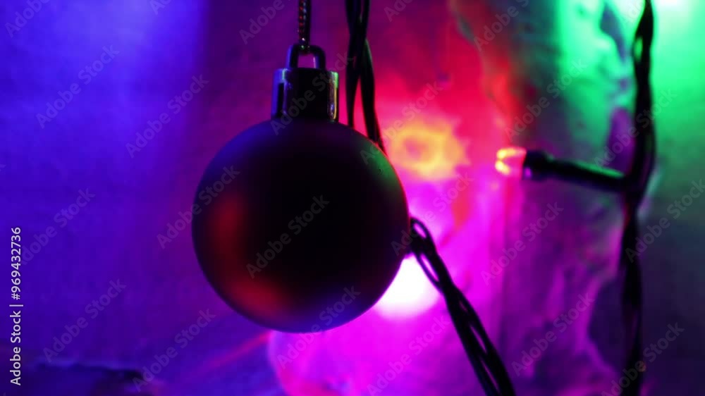 Una toma de cerca de una bola de navidad guindada en varias luces de colores en una pared de color blanco. Decoración de navidad y fin de año