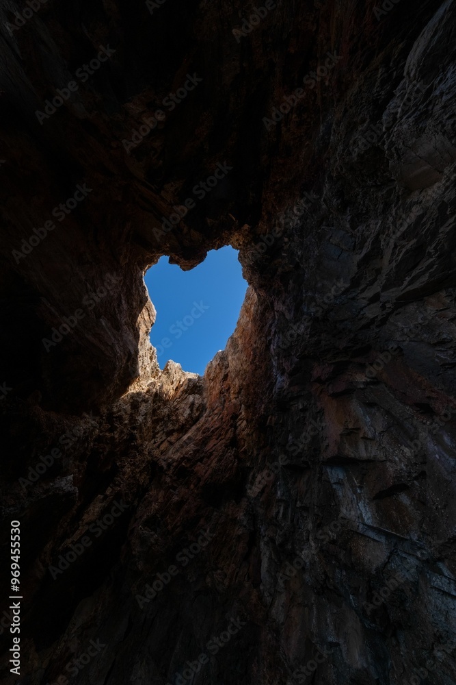 Vertical low angle shot of a cave opening with a view of the blue sky above in Zakynthos, Greece Vertical low angle shot of a cave opening with a view of the blue sky above in Zakynthos, Greece