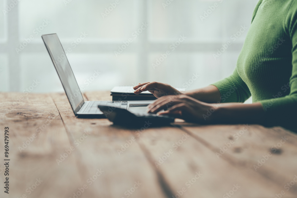 Fototapeta premium Focused Work at Home Office: A close-up of a woman's hands diligently working on a laptop, showcasing the modern home office environment with natural light streaming through the window. The image evo