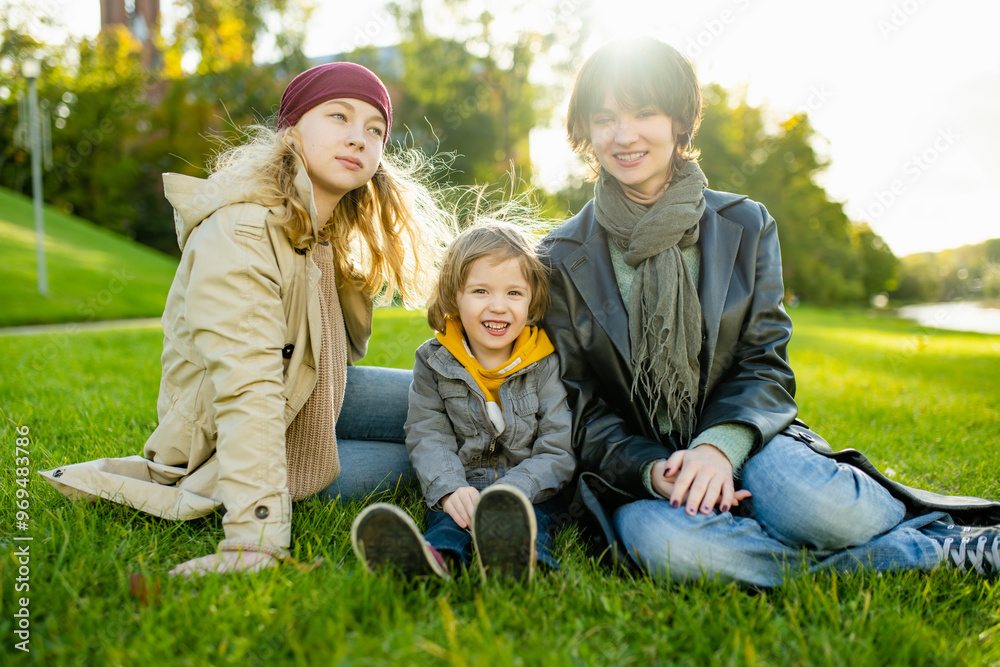 Fototapeta premium Two big sisters and their toddler brother having fun outdoors. Two young girls with a toddler boy on autumn day.