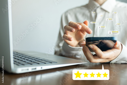 A man is using a cell phone while sitting at a desk with a laptop