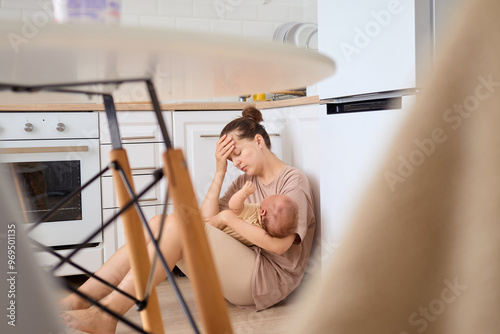 Fotografie Desperate woman sitting in the kitchen with her newborn son or daughter experien