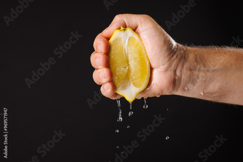 Фотография Squeezing fresh lemon juice on dark background, hand squeezing fresh lemon juice
