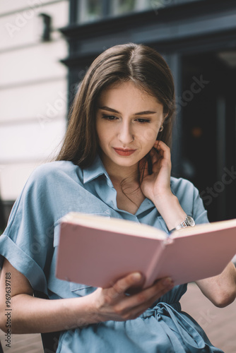 Gorgeous lady in stylish dress being high on book at cafe veranda