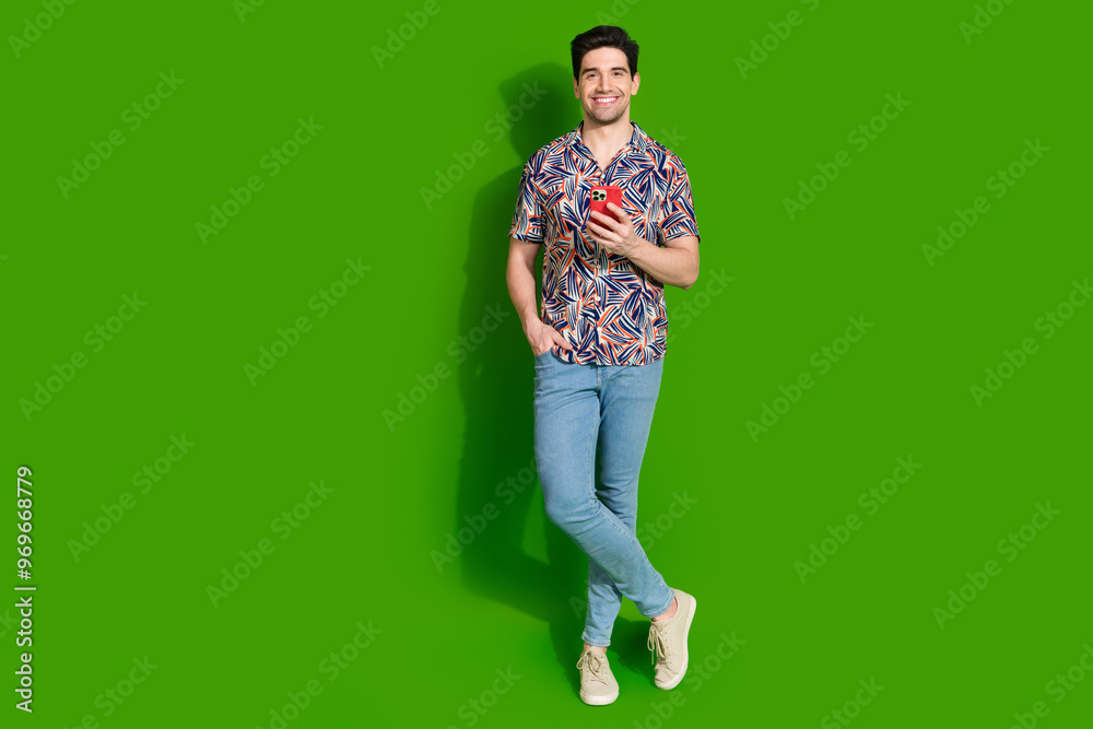 Full size photo of clever guy dressed print shirt jeans hold smartphone stand near offer empty space isolated on green color background Full size photo of clever guy dressed print shirt jeans hold smartphone stand near offer empty space isolated on green color background