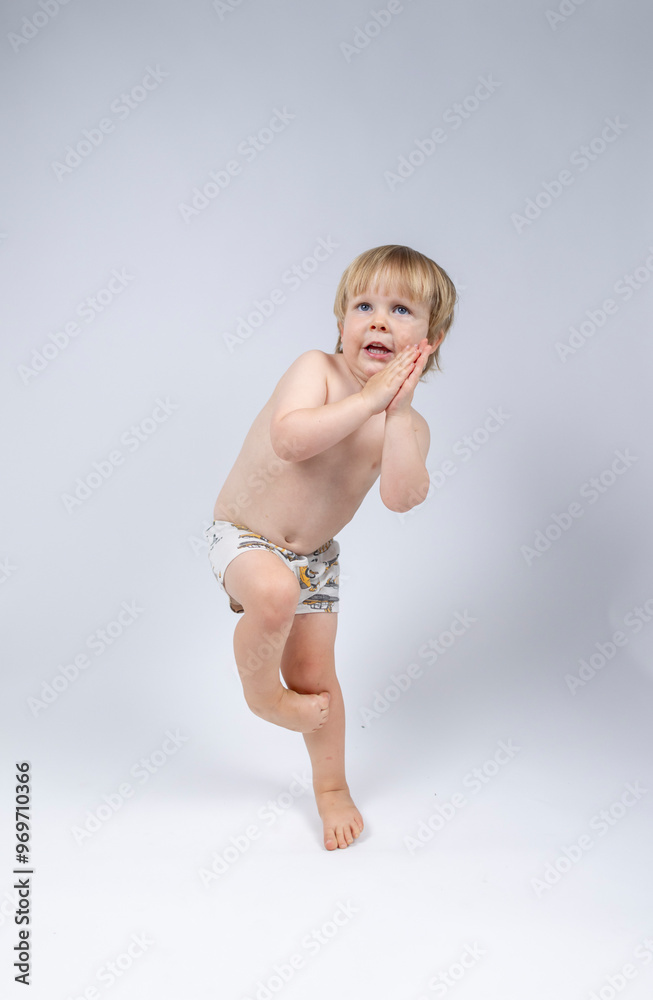 Naklejka premium A young toddler plays on a white backdrop in a photo studio.