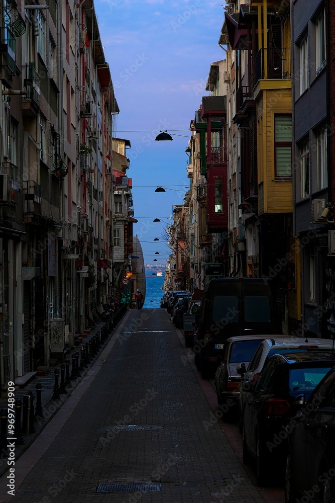 Street in a city with parked cars on both sides leading to a view of the Basfor and ships Street in a city with parked cars on both sides leading to a view of the Basfor and ships