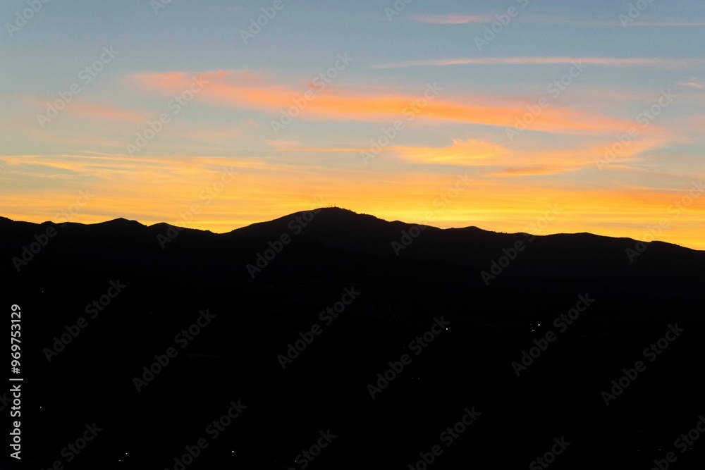 Silhouette of mountains against a vibrant sunset sky with orange and blue hues Silhouette of mountains against a vibrant sunset sky with orange and blue hues