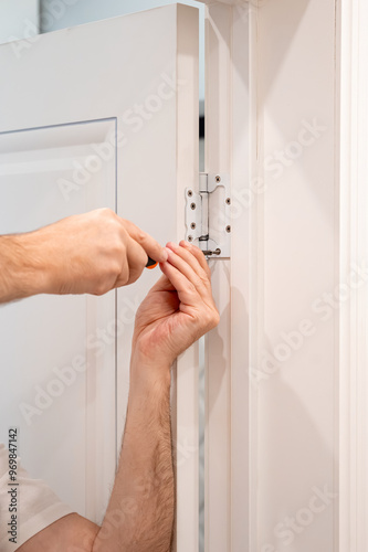Obraz na płótnie Man using a screwdriver to adjust a door hinge, close-up of hands performing home renovation and repair work w salonie