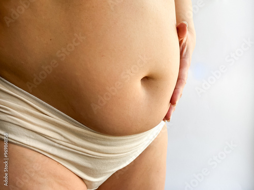 Pregnant belly in beige underwear with hand touching. Close up photography for maternity, pregnancy, and motherhood concept. Design for healthcare, prenatal care and wellness.