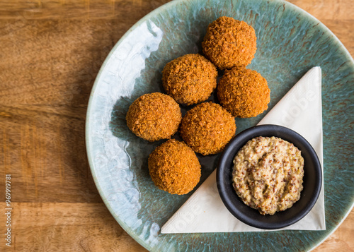 Top view of traditional Dutch bitterballen with mustard on a plate on a wooden table