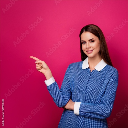 portrait of a businesswoman smiling, wearing ablue dress showing something on the empty magenta wall behind her  photo