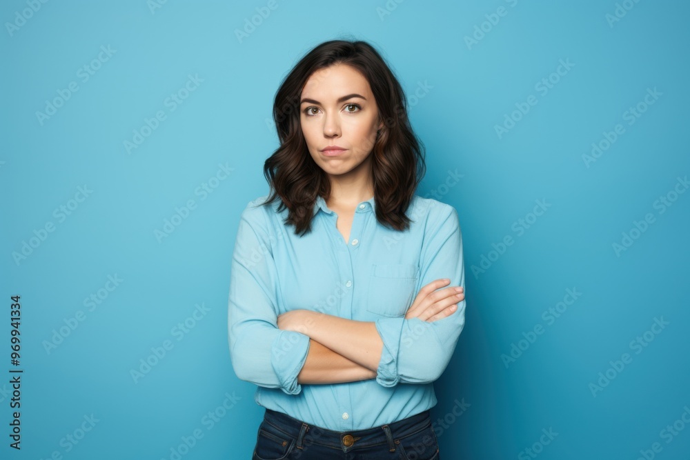 Confident woman against a blue background, crossing her arms and looking straight ahead with a serious expression. Confident woman against a blue background, crossing her arms and looking straight ahead with a serious expression.