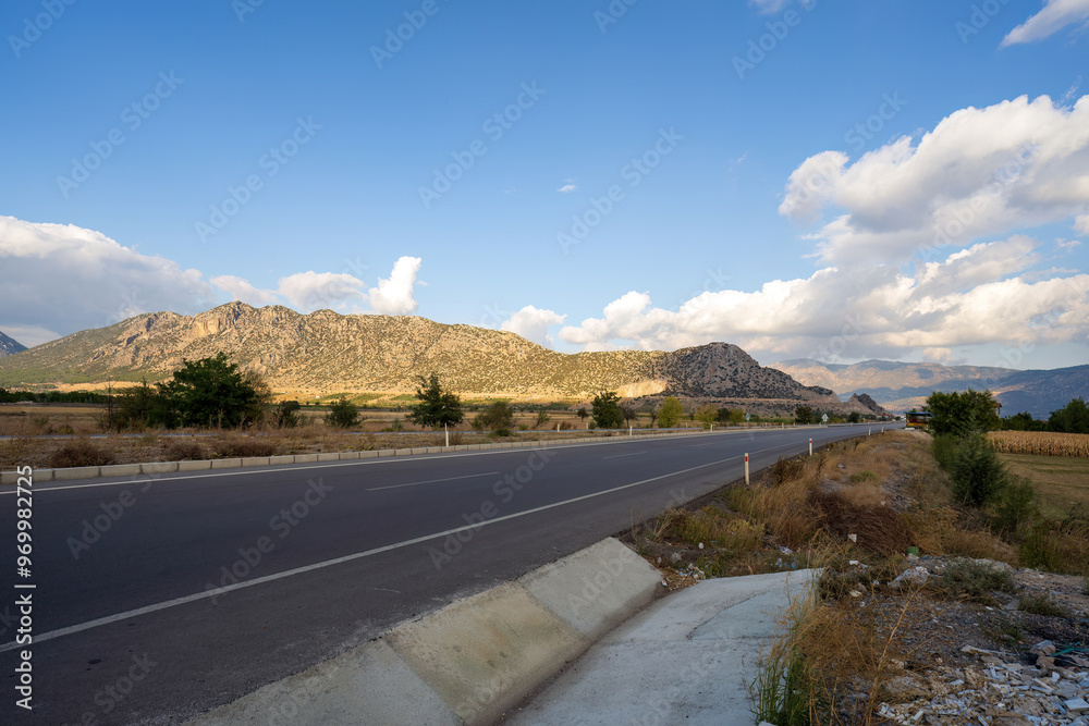 A long, straight highway in Turkey stretches out towards the distant mountains under a clear blue sky, offering a sense of freedom and open space.