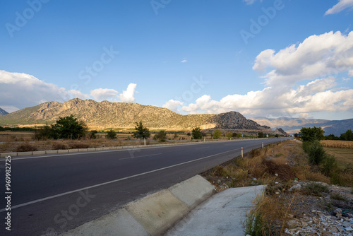 Obraz na płótnie A long, straight highway in Turkey stretches out towards the distant mountains under a clear blue sky, offering a sense of freedom and open space. w salonie