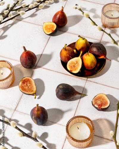sliced figs, candles and pussy willows on a white tile