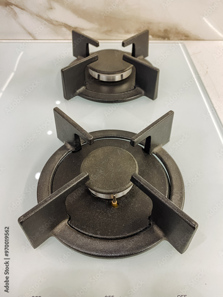 This image features a closeup view of two gas burners positioned closely on a pristine white stove top, showcasing the intricate details of the burners against the clean background This image features a closeup view of two gas burners positioned closely on a pristine white stove top, showcasing the intricate details of the burners against the clean background