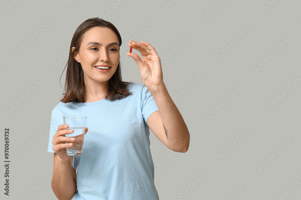 Pretty young woman with pill and glass of water on grey background Pretty young woman with pill and glass of water on grey background