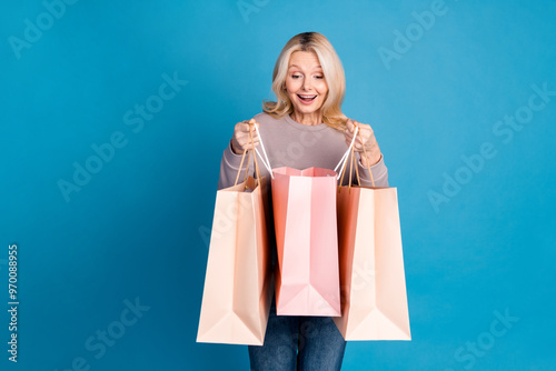 Photo portrait of lovely senior lady hold peek shopping bags dressed stylish gray garment isolated on blue color background