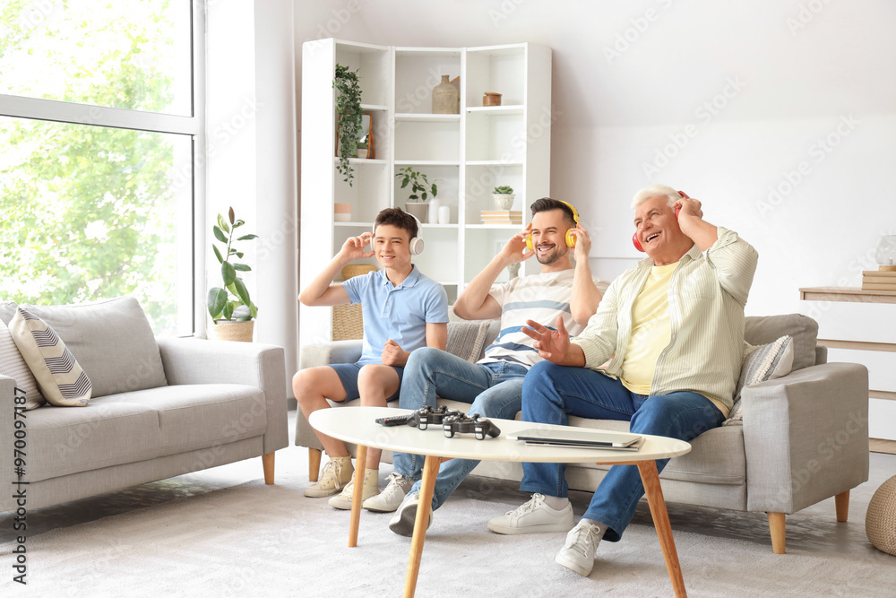 Teenage boy with his dad and grandfather in headphones sitting on sofa at home Teenage boy with his dad and grandfather in headphones sitting on sofa at home