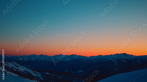 A sunset over a snowy mountain range with the peaks glowing in the last light of the day and the sky transitioning from orange to deep blue.