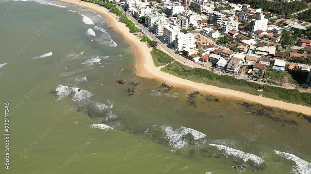 Imagem aérea da praia de Castelhanos em Anchieta, em uma manhã ensolarada. Praia deserta, ondas do mar e barracas na areia.